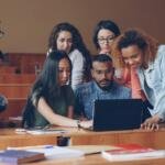 University students working together on a laptop in a classroom, illustrative stock photo for AI education partnership